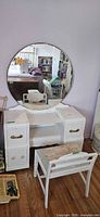 Front view of white wooden dressing table with round mirror and stool