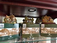 Three Lilliput Lane figures placed on top of their original green and white boxes with vintage village image.