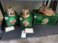 Three Lilliput Lane figures displayed on their original green boxes labeled Britain's Heritage, including Mickelgate Bar York, Tower of London, and Glamis Castle models.