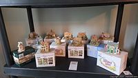 Full view of the collection arranged on a shelf showing 12 miniature cottages, some on original boxes.