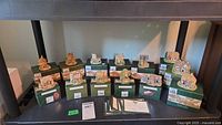 Shelved display of 13 boxed and unboxed Lilliput Lane miniature cottages with green packaging