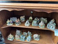 Full view of 22 small Lilliput Lane miniature cottage figures displayed on wooden shelves, showing detailed roofs, doors, windows, and scenic miniature elements.