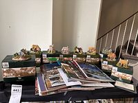 Overall view of nine Lilliput Lane figurines in original green boxes arranged alongside multiple Lilliput Lane catalogues on a surface.