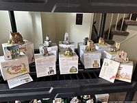 Multiple Lilliput Lane miniature figures displayed on and around original boxes showing different model building figures and their deeds.