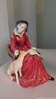 Front view of figurine showing seated woman in red dress reading a book with dog at her lap