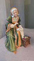 Front view of seated Anne of Cleves figurine in green and gold gown embroidery