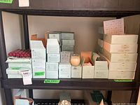 Wide shelf view showing multiple stacked boxes of taper candles, tea lights, votives, and jarred candle holders all in original packaging.