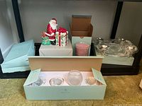 Lot of Partylite candle and holder items arranged on shelf including Santa holder, glass holders, candle boxes and hurricane jar candle.