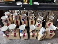 Overview photo showing 14 Peter Jones Aynsley royal commemorative mugs on original boxes arranged in rows, featuring various royal portraits and designs.