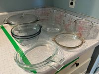 Photo showing various Pyrex glass measuring cups with red printed measurements, multiple clear glass bowls, and one large covered casserole dish on countertop.