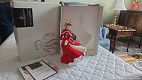Porcelain figurine with original box and certificate on a quilted surface.