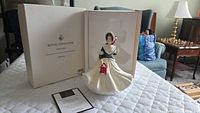 Wide shot of the Royal Doulton Christmas Day figurine with original box and certificate shown on a quilted surface.