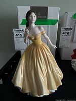 Front view of the Royal Doulton Elizabeth porcelain figurine in a yellow ball gown with original box behind.