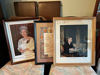 Three framed royal-themed prints including a portrait of Queen Elizabeth II, King George VI, and a Royal Family Tree print arranged together on furniture.