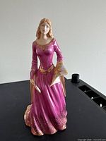 Front view of the Lady of Shalott figurine showing the detailed purple dress with gold accents and the figure holding a scroll and a small object.