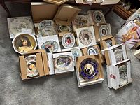 Photo showing multiple Royal Family collector plates arranged in original boxes on the floor.