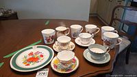 Full view of the lot including teacups, coffee mugs, saucers, and decorative plate arranged on a wood table.