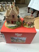 Front and left side view of the two Lilliput Lane miniature buildings on their original box, showing the Edzell Summer-house and smaller Wash Day cottage with detailed stone textures and landscaping.