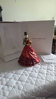 Porcelain figurine standing beside its original white Royal Doulton box, showing the full skirt and gift held in hands.