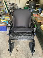 Front view of black wide wheelchair showing padded seat, footrests, armrests, and metal frame.