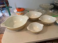 Set of four vintage Pyrex nesting mixing bowls in Homestead Cinderella pattern arranged on a table with other kitchen items in the background.