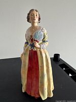 Front view of the figurine depicting woman in yellow gown holding a fan, showing detailed face and dress