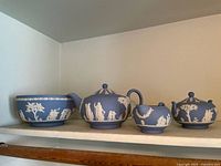 Four-piece Wedgwood Jasperware set on shelf showing bowl, teapot, creamer, and sugar bowl in classic blue with white relief decorations