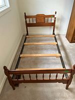 Front view of vintage wood veneer twin bed frame showing headboard, footboard, and wooden slats over metal frame supports.