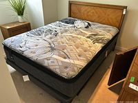 Full view of bed with wood veneer headboard, metal frame, and mattress with floral geometric upholstery pattern.