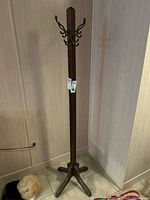 Full view of the wood coat rack showing the metal hooks at the top, vertical wooden post, and base with four legs.