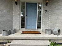 Five concrete bottomless planters arranged on a porch step, matching in design and size, showcasing their exterior appearance and scale near a door.