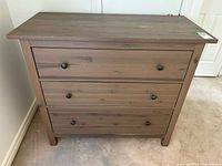 Front view showing three drawers with round metal pulls and laminate wood finish.