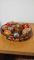 Multiple decorated Ukrainian pysanky Easter eggs and one wooden egg displayed inside a colorful ceramic bowl.