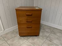 Front view of wooden laminate file cabinet showing three drawers and flat top
