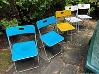 Set of six folding chairs outdoors on stone patio, three colors visible: blue, yellow, white.