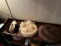 Top view of three vintage ladies hats placed on a wooden tray, showing textures, shapes and decorative details.