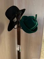 Two hats displayed on a wooden stand, a black hat and a green hat hung on opposite sides.
