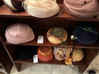 Photo of wooden shelving with multiple vintage ladies hats from the 1950s-1960s in various colors and materials including netted cream, green woven, blue with florals, orange, and others.