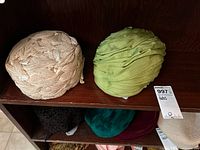 Two vintage ladies hats displayed on a wooden shelf, one beige cord hat and one green shantung hat.