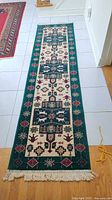 Full view of the entire runner rug showing the length, fringe ends, green border and patterned central field.