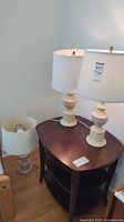 Three ceramic table lamps, two matching and one slightly taller, all with white drum shades.