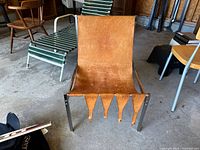 Front view of the leather and chrome framed chair, showing the worn tan leather seat and the leather straps hanging at the front bottom edge of the seat.