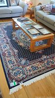 Wide view of machine made synthetic rug 6'x9' with floral pattern in living room setting under a glass-top wooden coffee table between gray couches