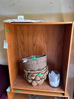 Front view of a laminate shelving unit showing wood grain laminate finish, open front, empty space for shelves, with woven baskets and plastic containers inside (not included).