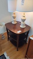 Dark brown wood side table with triangular rounded shape and two white lamps on top