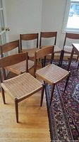 Six teak chairs arranged in dining area showing teak frames and woven rush seats