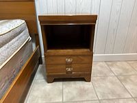 Photo of the vintage wooden night side table next to a bed, showing front view with two drawers and open upper compartment