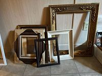 Five wood frames including large ornate gold frame and four smaller assorted wood frames with different finishes and decorative features.