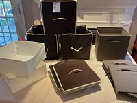 Overall view showing 12 fabric storage bins, some folded, some fully opened, colors brown exterior and white interior with beige edges