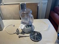 Full view of Black+Decker electric food processor with clear bowl, power base, and attachments laid out on table.